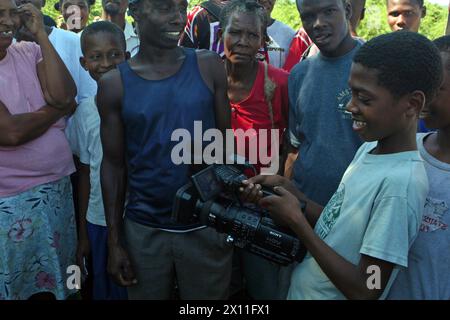 A group of Haitians from Cotes De Fer watch as a child plays with a video camera, Jan. 21.Marines and Sailors from the 22nd MEU set up a temporary relief-supply distribution point near Cotes de Fer, Haiti, bringing in bottled water and food for distribution to internally displaced Haitians. The 22nd MEU, embarked aboard the ships of the Bataan Amphibious Ready Mission, is deployed in support of relief operations in Haiti. Stock Photo