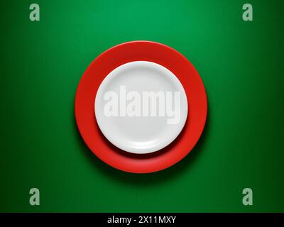 Food background. Empty ceramic white plate over a red plate on green background. Stock Photo