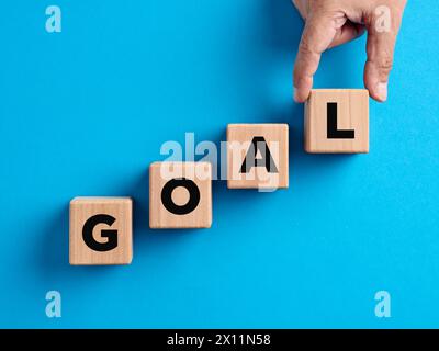Goal achievement, goal setting, business objectives, growth and success concepts. Hand arranges wooden cubes with the word goal. Stock Photo