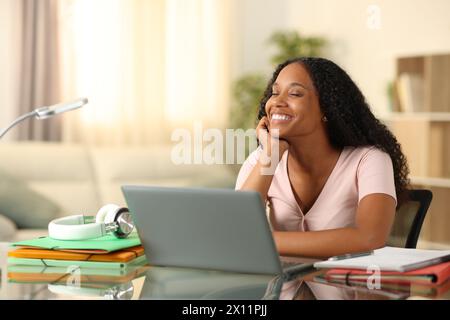 Happy black student relaxing and dreaming sitting at home Stock Photo
