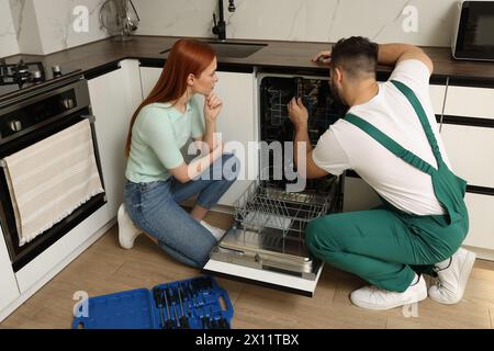 Woman looking how serviceman repairing her dishwasher in kitchen Stock Photo