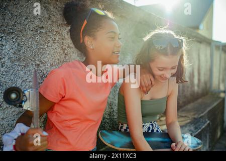 Teenager girl best friends with skateboards spending time outdoors in city during warm summer holiday day. Stock Photo