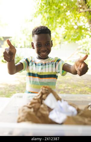 African American boy giving thumbs up, smiling, in backyard at home while recycling Stock Photo