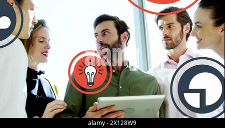 Image of multiple icons over diverse coworkers standing and discussing on digital tablet Stock Photo