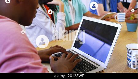 Image of multiple profile icons over diverse coworkers discussing and working on laptop Stock Photo
