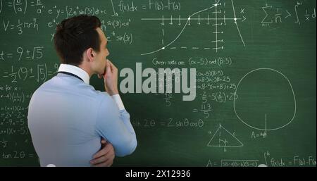 Image of head and shoulders back view of a Caucasian man with hand on chin facing a green chalkboard Stock Photo