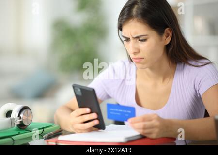 Worried student buying online with credit card and phone at home Stock Photo