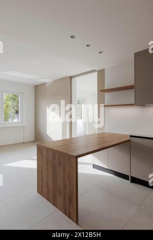 Wooden kitchen table attached to the wall. Behind asi sees an open door with a beam of light coming in through a window from the back. Stock Photo