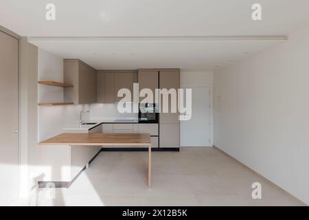 Front view of a new kitchen with a sturdy wooden table in front. Very large space or room with white walls. Stock Photo