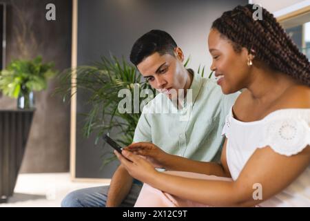 Biracial colleagues looking at smartphone together in a modern business office Stock Photo