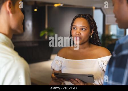 Diverse group discussing in a modern business office, biracial woman holding tablet Stock Photo