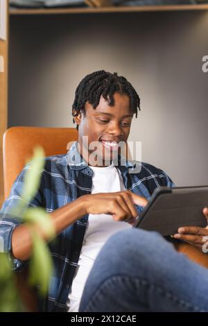 African American man sitting in a modern business office, using a tablet with a smile Stock Photo