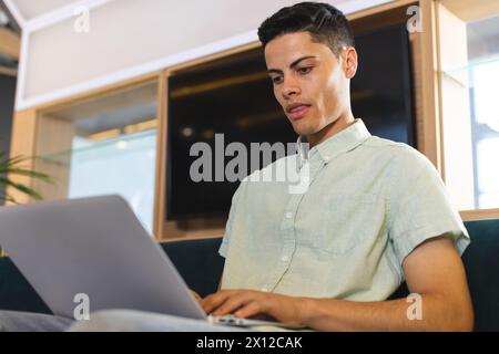 Biracial young man working on laptop, sitting on couch in a modern business office Stock Photo