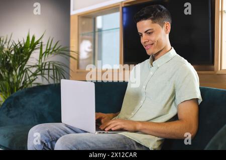 Biracial young man using laptop on blue sofa in a modern business office Stock Photo