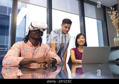 Diverse group of colleagues exploring virtual reality and using laptop in a modern business office Stock Photo