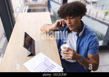 A young biracial man with curly brown hair is talking on the phone in a modern business office Stock Photo