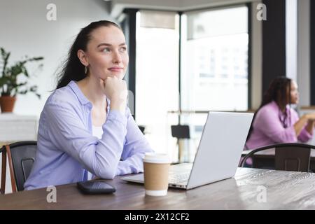 Biracial woman with laptop looking thoughtful at cafe Stock Photo