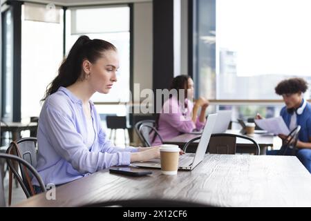 Caucasian woman typing on laptop in a modern business office, biracial woman and man talking Stock Photo