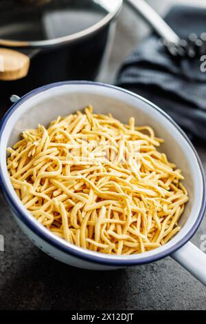 Uncooked spaetzle pasta in colander on a kitchen table. Stock Photo