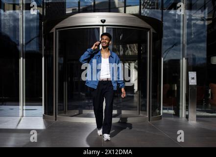 Smiling young man calling with phone leaving entrance modern bus Stock Photo