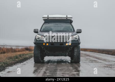 Grey Offroad Vehicle With Roof Tent On Wet Muddy Road Stock Photo