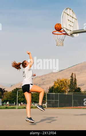 Girl with pony tail jumping in air playing basketball Stock Photo