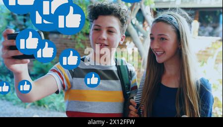 Image of media icons over happy caucasian schoolkids using smartphone Stock Photo