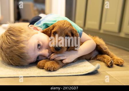 Boy and puppy cuddle on floor in heartwarming hug Stock Photo