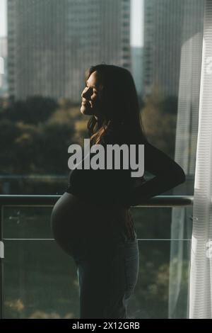 Pregnant women enjoying the sun standing near the window Stock Photo