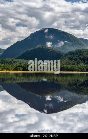 Summer reflections on the calm flat water at the Stangvikfjord with a view of the nature reserve and a farm in the mountains of Trollheimen, Norway Stock Photo