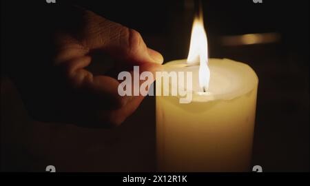 Close-up of a man's hands lighting a candle with a match in the dark, it burning Lighting a candle with match over darkness home. Stock Photo