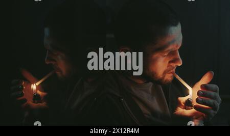 Handsome bearded man smoking cigarette sitting in the dark room. Hipster with lighter and cigarette. Closeup. Stock Photo