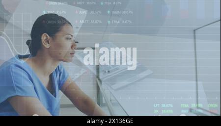 Image of graphs, trading board and calculator on table over biracial thoughtful female nurse Stock Photo