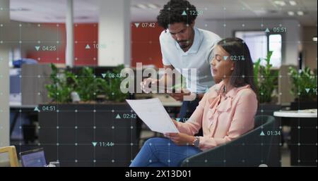 Image of changing numbers and icons over diverse coworkers discussing reports in office Stock Photo