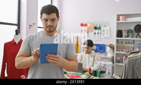 Two men working in a tailor shop, with one using a tablet and the other sewing. Stock Photo