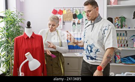 Two tailors, a woman and a man, collaborating in a tailor shop with colorful fabrics and a red dress on a mannequin. Stock Photo