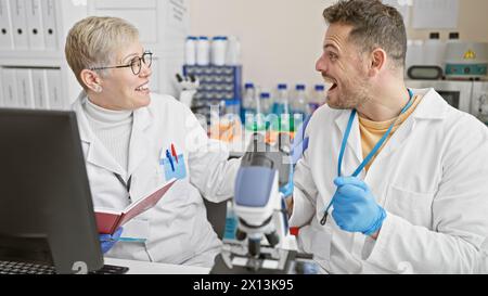A man and woman, both smiling scientists, revel in teamwork at a bustling laboratory research center. Stock Photo