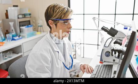 A focused hispanic woman works with a microscope in a well-lit laboratory, embodying professionalism and expertise. Stock Photo