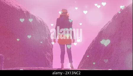 Image of glowing spots and hearts over caucasian woman standing on rock Stock Photo