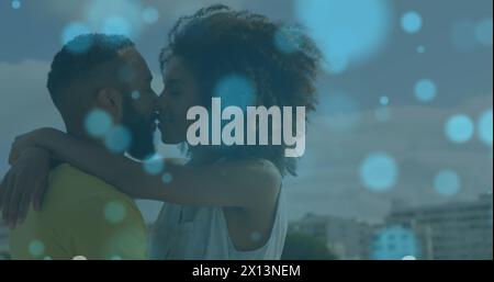 Image of light spots over african american couple embracing and kissing at beach Stock Photo