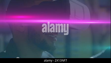 Image of blue and pink light trails moving over biracial man wearing vr headset Stock Photo