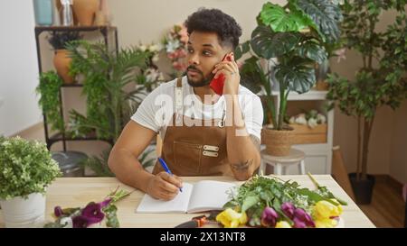 An african american man in a florist shop talking on the phone while taking notes surrounded by plants. Stock Photo