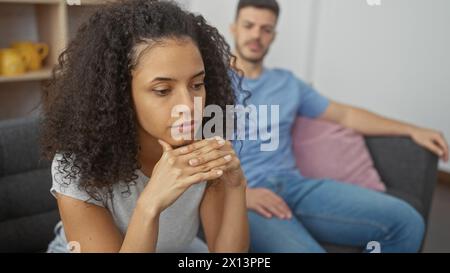 A contemplative woman and a man sit apart on a couch in a modern living room, suggesting tension in their relationship. Stock Photo