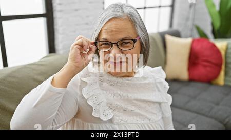 A smiling senior woman adjusting her glasses, comfortable in her modern living room. Stock Photo
