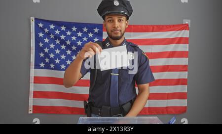African american policeman holding card in front of us flag at polling station Stock Photo