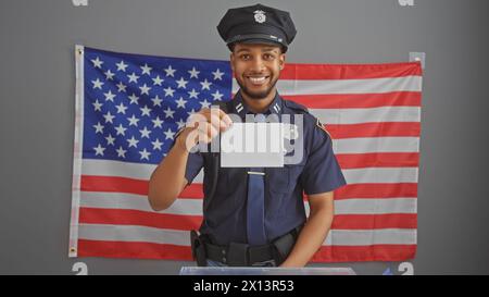 Smiling african american policeman holding blank card in front of us flag Stock Photo