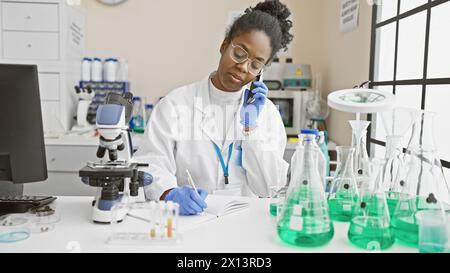 African american woman scientist analyzing samples while talking on the phone in a laboratory Stock Photo