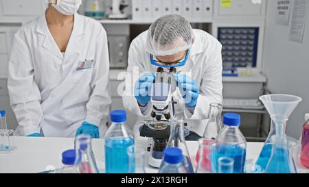 Two scientists wearing medical mask and gloves using microscope at laboratory Stock Photo