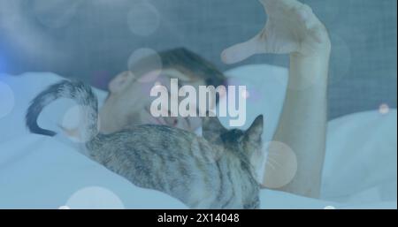 Spots of light against caucasian man playing with his cat while sleeping on the bed at home Stock Photo