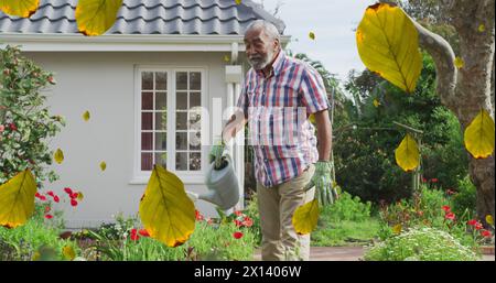 Multiple leaves icon falling against african american senior man watering plants in the garden Stock Photo